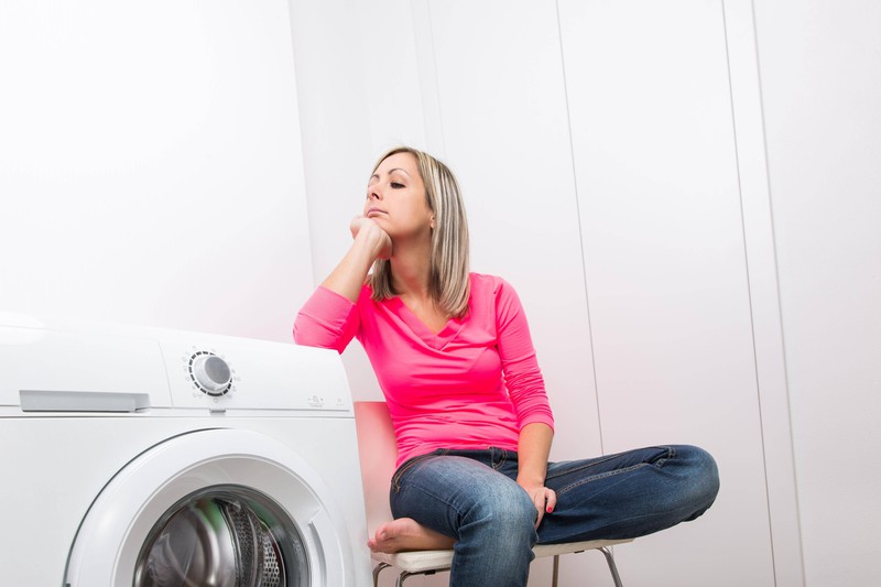 A woman is waiting for the laundry to be done because she didn't use quick wash.