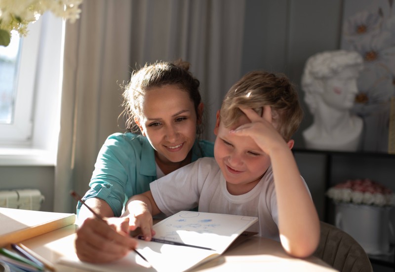 A babysitter helps a kid doing his homework.