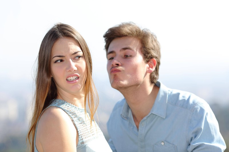 A woman turns away from a guy trying to kiss her.