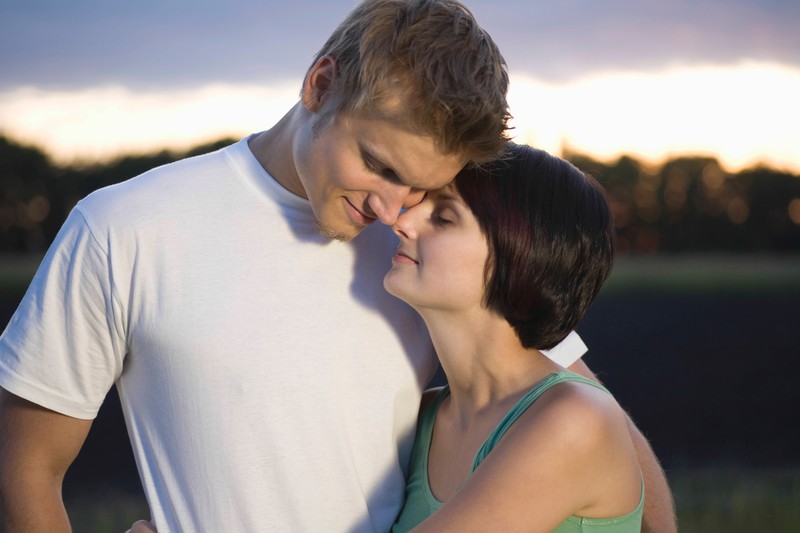 Couple stand embracing with eyes closed in evening