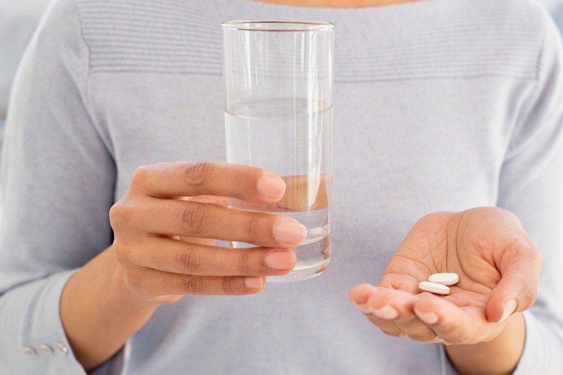 A woman holds pills and a glass of water in her hands