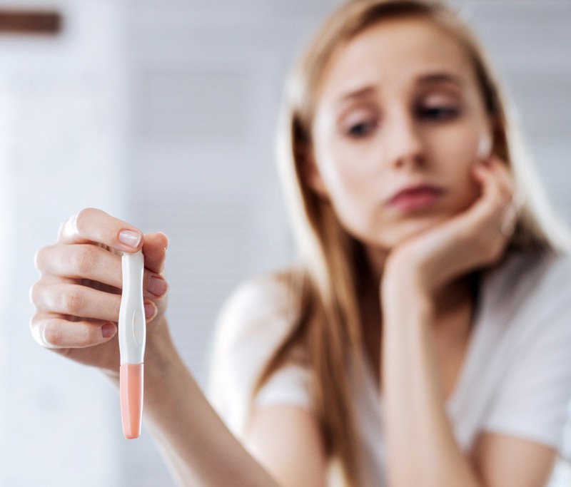 Young woman holds pregnancy test in her hands and her look is sad.