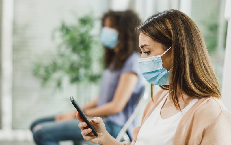Young woman with mouth mask sits in the waiting room at the doctor's office.