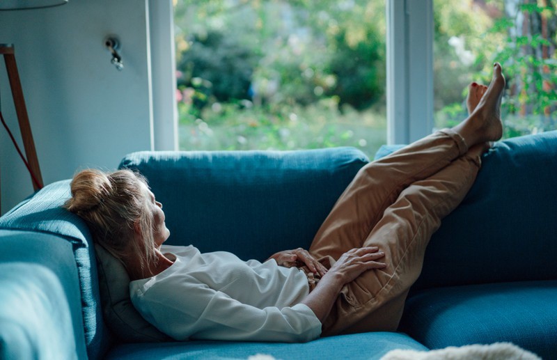 Une femme s'allonge pensivement sur le canapé et regarde dehors par la fenêtre.