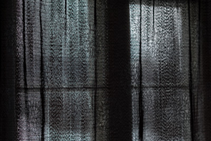 Closeup of a black, translucent curtain closed in front of a window