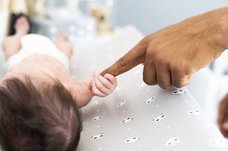 Close-up of newborn baby grabbing father s finger on changing table