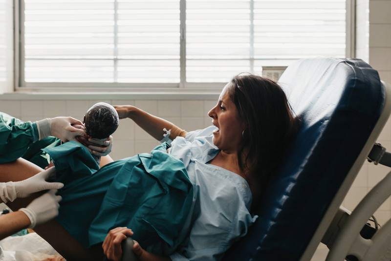 Resilienz Strained female grasping handle and grunting in pain while giving birth to baby on medical chair in modern hospital